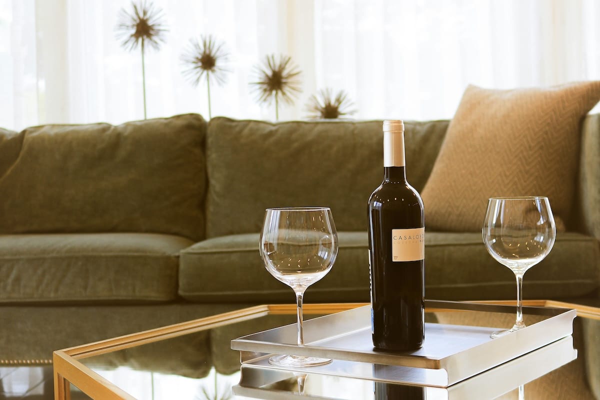 Two empty glasses of wine sitting on a coffee table next to an unopened bottle of wine