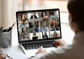 Rear close up view of female employee brainstorm talk on video call with diverse colleague on laptop. Woman speak engaged in team group discussion, have webcam company online meeting or briefing.