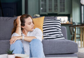 Young depressed woman sitting on sofa in living room. She feeling sad and worried suffering depression in mental health. Problems and broken heart concept