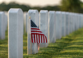 Military burial headstones. Sarasota National Cemetery with rows of white tomb stones and USA flags on green grass. Memorial Day concept.